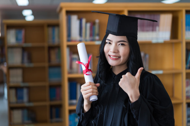 一名年轻快乐的亚洲女子大学毕业生穿着毕业礼服和帽子戴着面具持有学位证书，以庆祝她的教育成就在毕业典礼上。库存图片图片下载