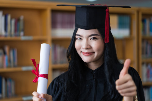 一名年轻快乐的亚洲女子大学毕业生穿着毕业礼服和帽子戴着面具持有学位证书，以庆祝她的教育成就在毕业典礼上。库存图片图片下载