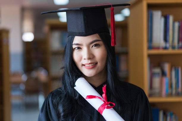 一名年轻快乐的亚洲女子大学毕业生穿着毕业礼服和帽子戴着面具持有学位证书，以庆祝她的教育成就在毕业典礼上。库存图片图片下载