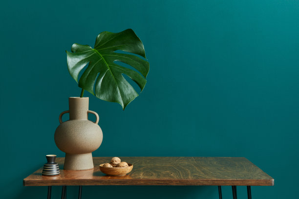 时尚概念的客厅内饰胡桃木桌子，热带叶花瓶，钟表和优雅的个人饰品在现代复古家居装饰。绿色的墙。副本的空间。图片下载