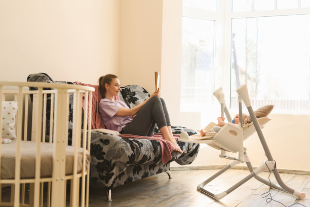 母亲把孩子放在孩子的电动摇篮里睡觉。做母亲和组建家庭的幸福图片下载