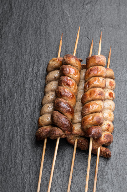 黑色石板背景上的木棍烤螺旋香肠图片下载
