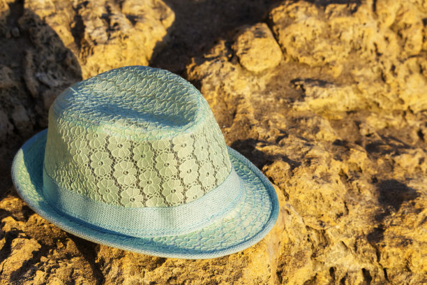 一个小孩的帽子从太阳熊的形式躺在沙滩上的岩石上，沙滩概念图片下载