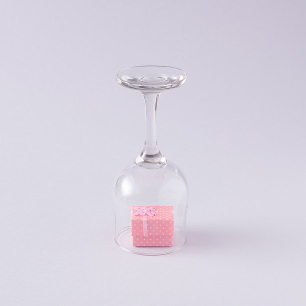 浅粉色礼盒，装在酒杯里。淡灰色的背景。最小的组合。图片下载