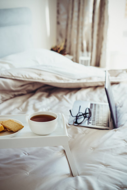 白色的木制托盘，配有一杯热茶或咖啡和饼干，背景是一台笔记本电脑。商务人士早餐。成功人士的早晨习惯。垂直的名片。副本的空间。图片下载