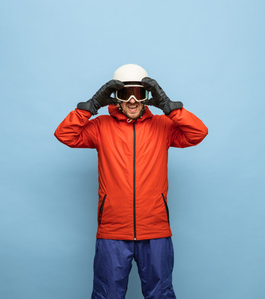 运动男子在明亮的滑雪服，头盔和护目镜孤立在蓝色背景。图片下载