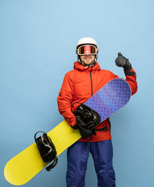 年轻男子在明亮的滑雪服和滑雪板摆出孤立的蓝色背景。图片下载