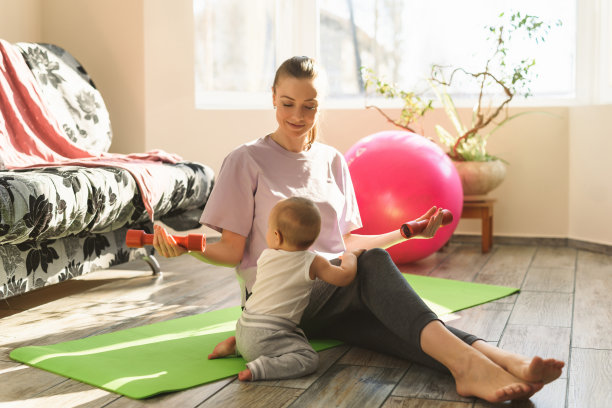 一个年轻的妈妈带着一个婴儿坐在运动垫上准备做运动。在家健身和瑜伽。闭关锁国则检疫摧毁图片下载