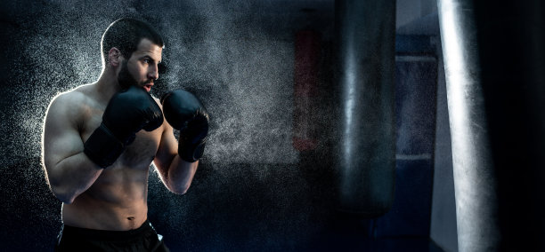 一名男性拳击手在拳击工作室击打一个巨大的沙袋。男子拳击手刻苦训练图片下载