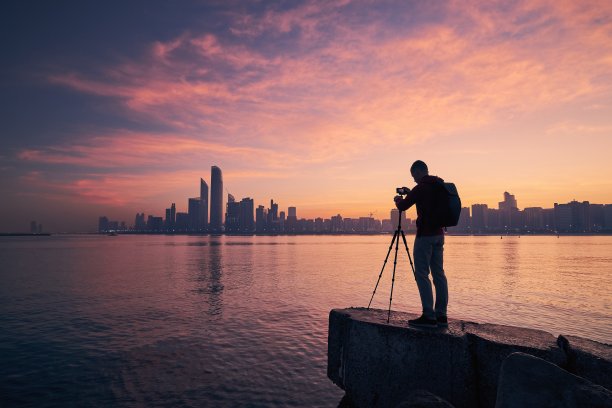 以城市天际线为背景，手持三脚架的摄影师轮廓图片下载