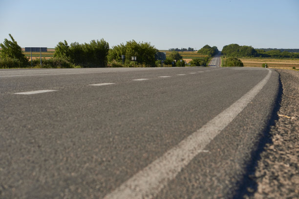 软焦点沥青路面与白色标记近距离从低镜头。模糊的乡村道路和田野与森林在夏天。高质量的照片。旅行、科技、自然的概念。图片下载