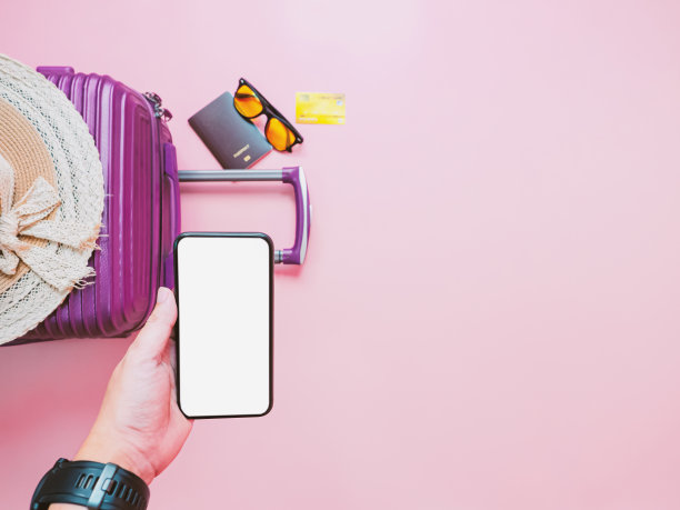 在线预订旅行和支付概念从智能手机和手提箱与粉红色的背景夏季系列。图片下载