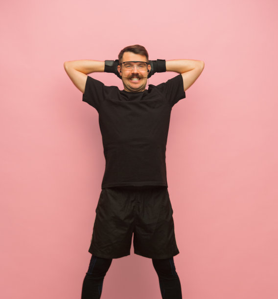微笑的男人在黑色运动服和眼镜孤立在粉红色的背景。图片下载