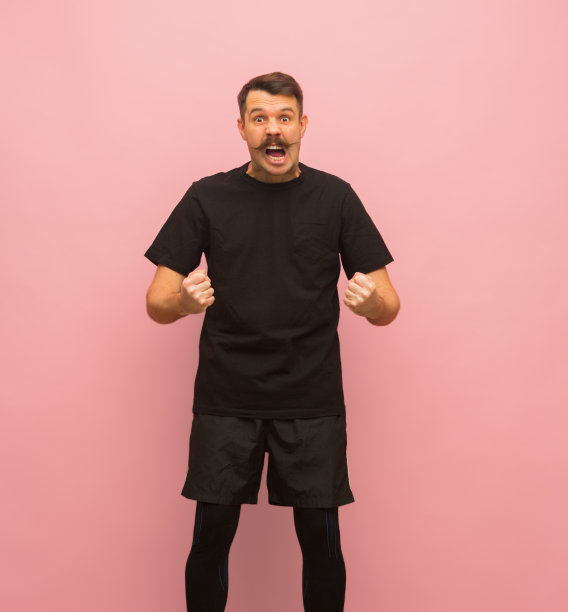 年轻的白人男子在黑色的运动服装孤立在粉红色的背景。图片下载