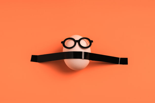 白色的鸡蛋，黑色的眼镜，橙色的背景。复活节假期的创意概念。平的。图片下载