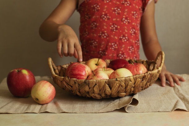 一个孩子拿着一个柳条篮子，里面装满了收获的苹果。秋天是收获的季节。自然产品。图片下载