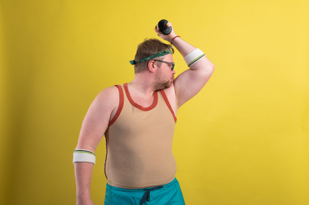 滑稽的胖子用哑铃做运动。超重。黄色背景图片下载