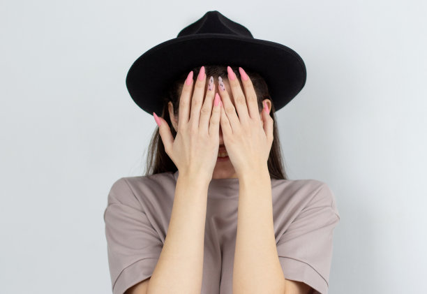 黑发女孩盖着她的脸与她的手，生活方式概念工作室照片在一个白色的背景。社交恐惧症的概念图片下载