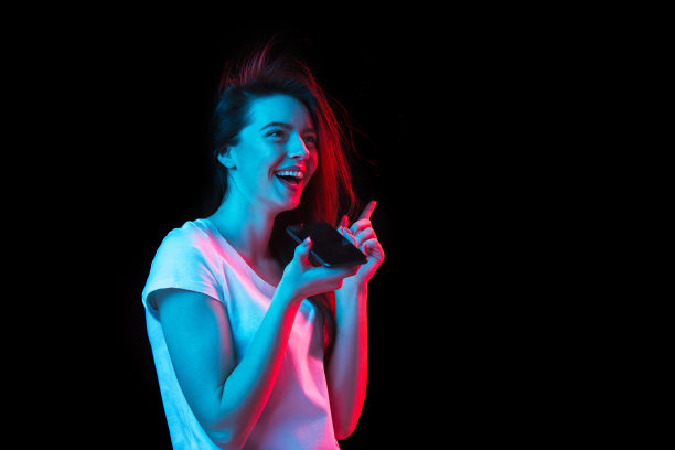 年轻美丽的女孩与智能手机孤立在霓虹灯的黑暗背景图片下载