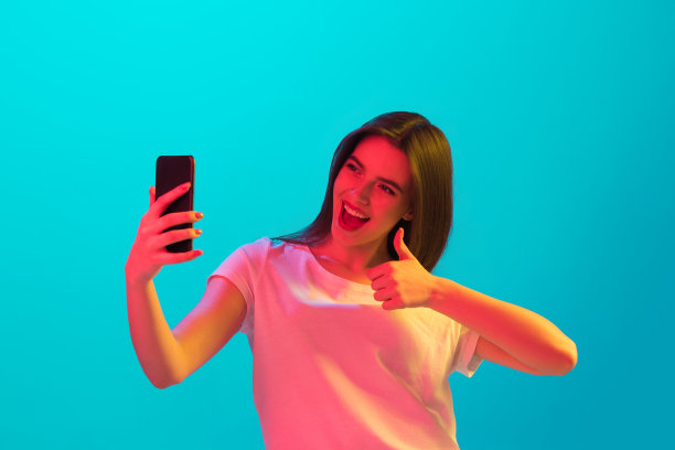 年轻美丽的女孩与智能手机孤立在蓝色背景霓虹灯图片下载