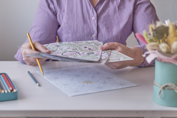 老妇手里拿着一支彩笔，画着成人涂色页。图片下载