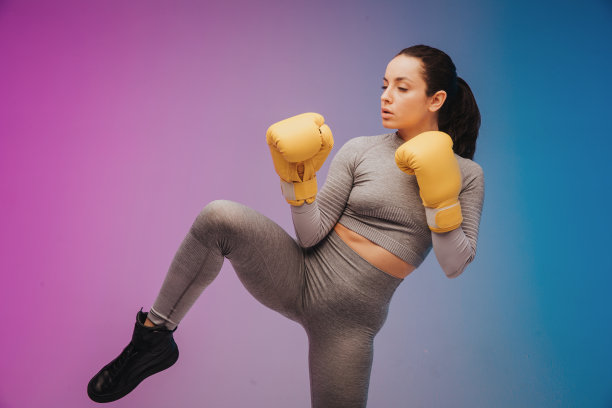 强壮的女运动员在拳击手套准备高踢的照片。隔离在霓虹灯梯度工作室背景。美丽的白人女人练习图片下载