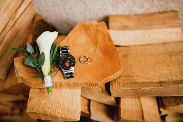 靠墙的木头上挂着结婚戒指，一个男人的手表和一个马蹄莲花胸花。图片下载