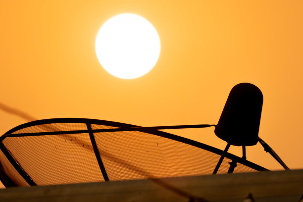 卫星技术碟式接收器在日出和金色的天空背景下，模糊的屋顶前景在阳光的光线图片下载