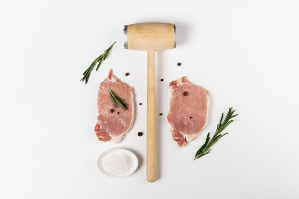 用迷迭香、盐和胡椒粉拌生猪肉。俯视图上的白色背景和厨房锤子图片下载
