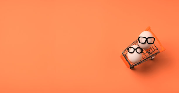 一对白色的鸡蛋，戴着黑色的眼镜，放在一个橙色背景的篮子里。复活节假日购物简约概念。春季出售。横幅。平的。副本的空间。图片下载