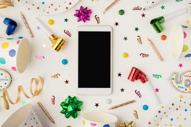 上面的照片杯子盘子、五彩纸屑、蜡烛、弓、空白的电话和聚会哨子孤立在白色的背景图片下载