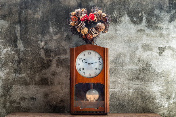 用干果做成的心形花环放在靠在水泥墙上的老式木钟摆上。“爱总有时间”的概念。图片下载