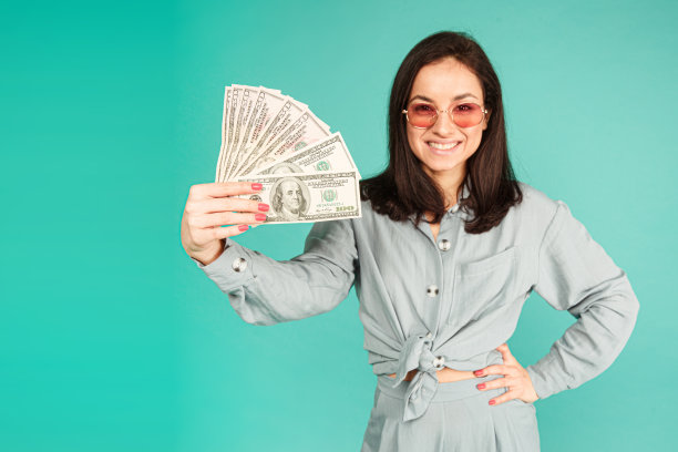 照片上戴着太阳镜的美女装着钱。身穿灰色衬衫，孤立的绿松石色背景图片下载