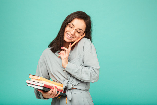 可爱的女性拿着书和打电话的照片。身穿灰色衬衫，孤立的绿松石色背景图片下载