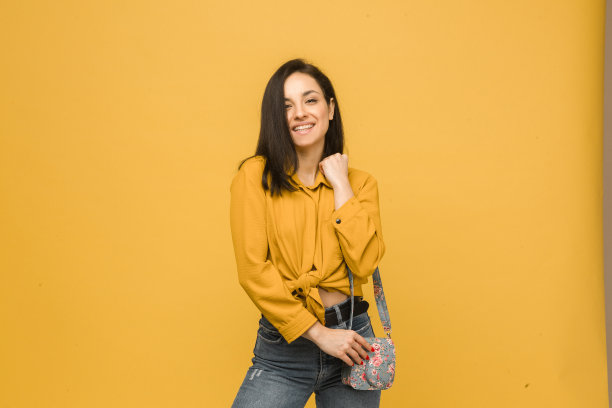 概念照片的年轻女性与钱包，微笑，看起来很高兴。身穿黄色衬衫，孤立黄色背景图片下载