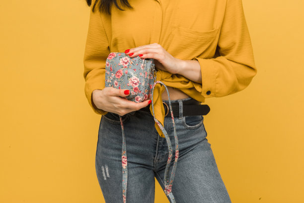 近距离照片的年轻女性持有她的钱包。身穿黄色衬衫，孤立黄色背景图片下载