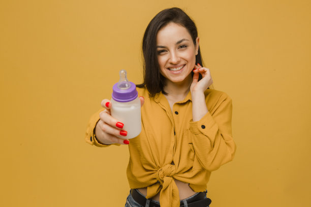 可爱的女性抱着婴儿奶瓶的照片。身穿黄色衬衫，孤立黄色背景图片下载