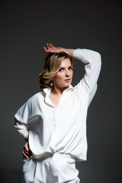 画室里一个灰色背景的漂亮女人穿着白裤子和白衬衫图片下载