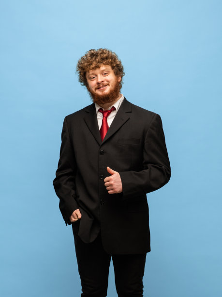 年轻的红发男子的肖像在黑色西装孤立在蓝色背景。图片下载