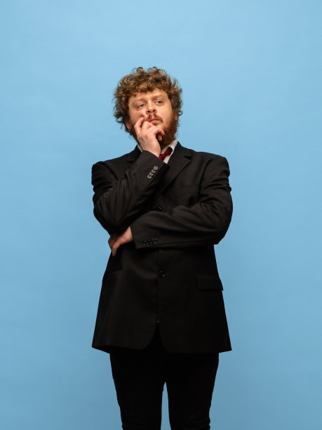 年轻的红发男子的肖像在黑色西装孤立在蓝色背景。图片下载