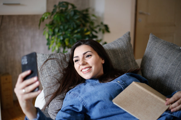 她的特写照片，她很漂亮，可爱，迷人，快乐，快乐的女孩躺在床上用app 5g发送照片。库存图片图片下载