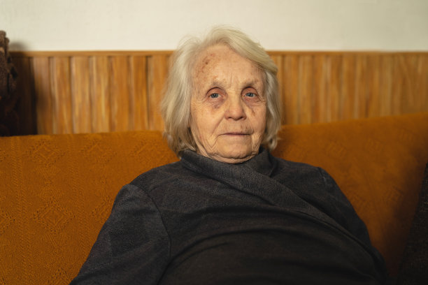 正面的观点肖像，一个年长的妇女退休老人坐在沙发床在家里看着相机-真实的人祖父母奶奶退休的概念图片下载