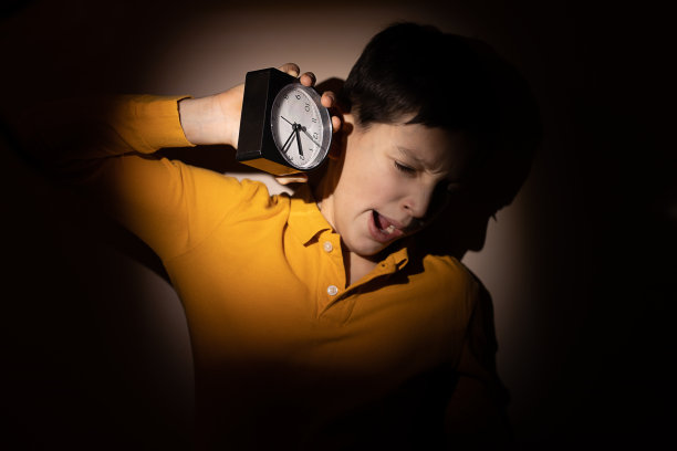 十几岁的小男孩手里拿着闹钟，在路上睡着了，晚上。儿童和青少年睡眠障碍的概念。强光，特写照片图片下载
