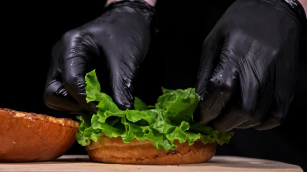 手工汉堡在黑色背景下烹饪。包括:酱汁，生菜，番茄，红洋葱，泡菜，奶酪，培根，空气面包和大理石肉牛肉。图片下载