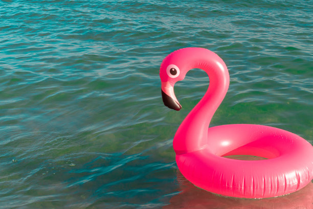 夏天有趣的海滩。粉红色的充气火烈鸟在蓝色的海水在夏季海洋海滩的背景。有趣的小鸟玩具的孩子。图片下载