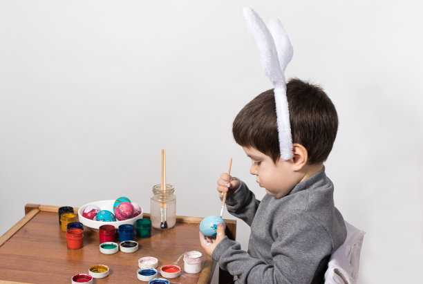 一个小男孩画水粉鸡蛋。为准备复活节，兴高采烈的孩子们画上了鸡蛋的颜色图片下载