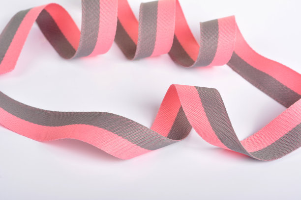 粉红色和灰色的棉带，卷筒上的纺织品。捆扎带和绳子石灰织带与卷曲在白色的背景。图片下载