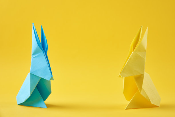 两个彩色的折纸兔子在黄色的背景上。复活节庆祝活动的概念图片下载