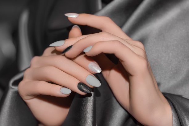 女性的手与银指甲设计。亮黑色指甲油美甲。女人的手在灰色的织物背景。图片下载