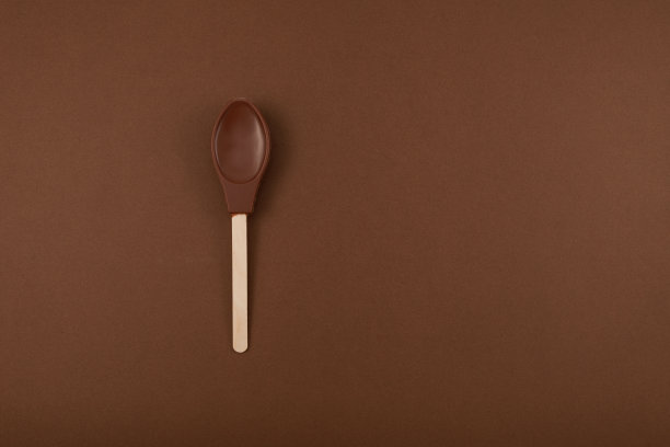 牛奶巧克力勺在棕色背景与复制空间。设计元素。可食用的奶昔勺子图片下载